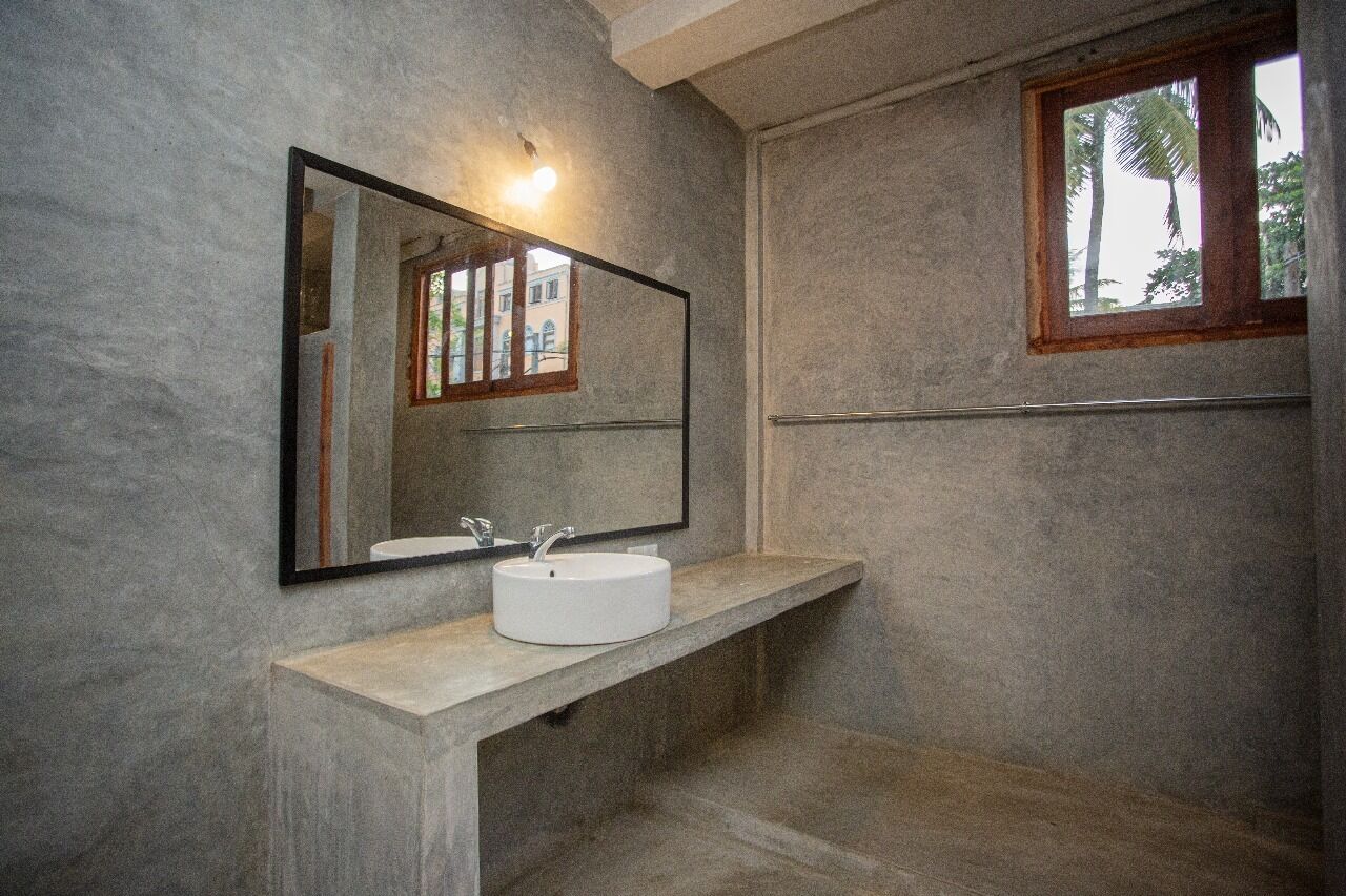 A bathroom with a white sink, a mirror, and a window with a view of palm trees.