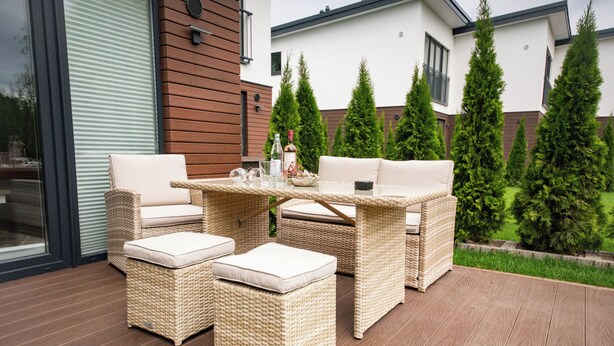 A wicker outdoor seating area with cushions, a table, and a bottle. - Baltic Village - Comforthaus (Damp)