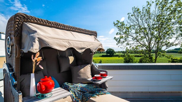 A covered outdoor seating area with a red teapot, a tray with red cups, and a colorful blanket. - Lovely apartment in Olpenitz with sauna (Olpenitz)