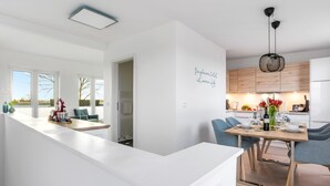 A modern kitchen with a dining area, white countertops, and a view through an open door. - Lovely apartment in Olpenitz with sauna (Olpenitz)