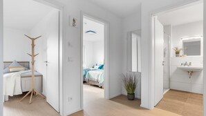 A modern hotel room with a wooden floor, a bed with a white headboard, a bedside table with a lamp, and a large mirror above the sink. - Lovely apartment in Olpenitz with sauna (Olpenitz)