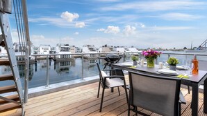 A rooftop terrace with a table set for two, overlooking a marina with boats and buildings. - Stunning ship in Olpenitz with sauna (Olpenitz)