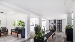 A spacious lobby with a modern design, featuring a seating area with chairs and tables, potted plants, and a large door with a security gate. - Casita Layla (Puerto Vallarta)