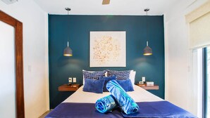 A modern hotel room with a large bed, two bedside tables, a wall-mounted abstract painting, and a window with blinds. - Casita Layla (Puerto Vallarta)