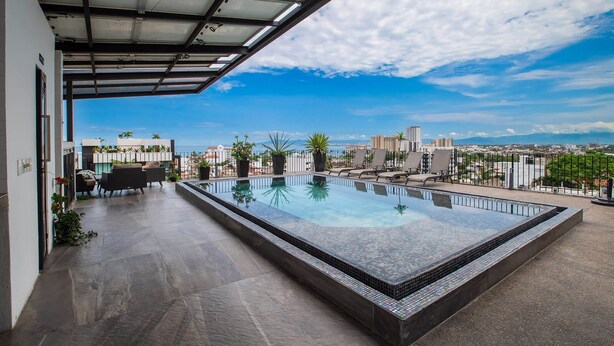 A rooftop swimming pool with a city view, surrounded by lounge chairs and potted plants. - Casita Layla (Puerto Vallarta)