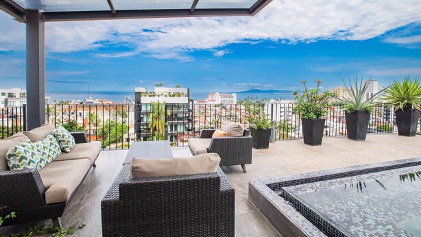 Une terrasse sur le toit, aménagée avec des espaces de détente en plein air, des plantes en pot et offrant une vue sur le paysage urbain.
