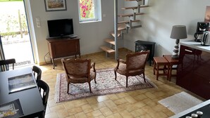 Un salon équipé d’un téléviseur, de deux fauteuils, d’un tapis, d’un escalier et d’un coin cuisine.
