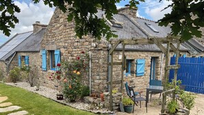 Une maison en pierre avec un jardin, une pergola et une clôture bleue.