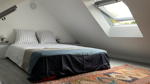 Une chambre avec un plafond en pente, un puits de lumière, un lit avec des coussins à rayures, une table de chevet avec une lampe et un tapis à motifs.