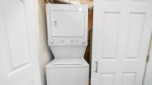 A compact, white laundry room with a built-in washer and dryer, a door, and a wall-mounted vent.
