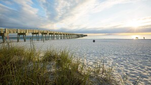 A beach with a pier extending into the water, a clear sky, and a sunset.