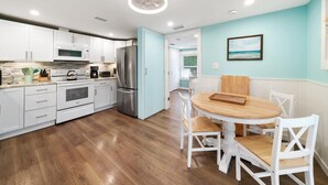 A modern kitchen with white cabinetry, stainless steel appliances, and a wooden dining table with white chairs.
