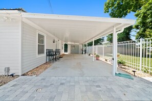 A covered patio with a table and chairs, a white fence, and a pathway leading to a door. - Beachside Hideaway | Near the Shore & Dog-Friendly (Panama City Beach)