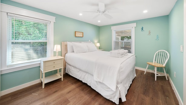 A bedroom with a bed, nightstands, a chair, a ceiling fan, and a window with blinds.
