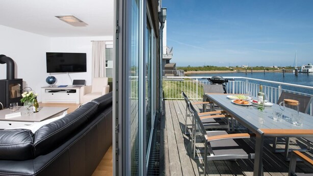 A modern living room with a black leather sofa, a flat-screen TV, and a dining area with a table set for two.
