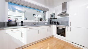 A modern kitchen with white cabinets, a stainless steel range hood, a microwave, and a built-in oven.