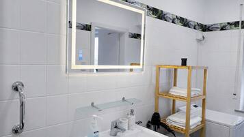 Un baño moderno con estante de vidrio, toallero de madera, lavabo blanco y espejo con marco iluminado.
