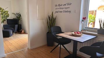 Ein modernes Interieur mit Essbereich, der einen Holztisch und schwarze Stühle, eine Wand mit einer dekorativen Beschriftung sowie einen Blick ins Freie durch ein Fenster zeigt.