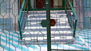 Eine Treppe führt zu einem Hauseingang, umgeben von einem Metallzaun mit grünem Rahmen.