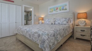 A bedroom with a bed, a ceiling fan, a nightstand, a lamp, a framed picture, and a sign above the door. - LIFE IS BETTER AT THE BEACH! ESTERO BEACH & TENNIS CLUB 603B! (Fort Myers Beach)