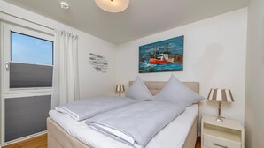 Une chambre à coucher avec un lit, une table de chevet, une lampe, un tableau et une fenêtre avec des rideaux.