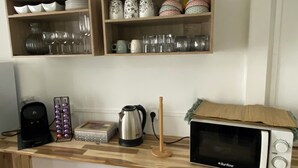 A kitchen counter with a microwave, kettle, and coffee maker. There are shelves above holding dishes and cups. - Mzelle Pipine à 2 Minutes de la Plage ! (Saint-Pierre)