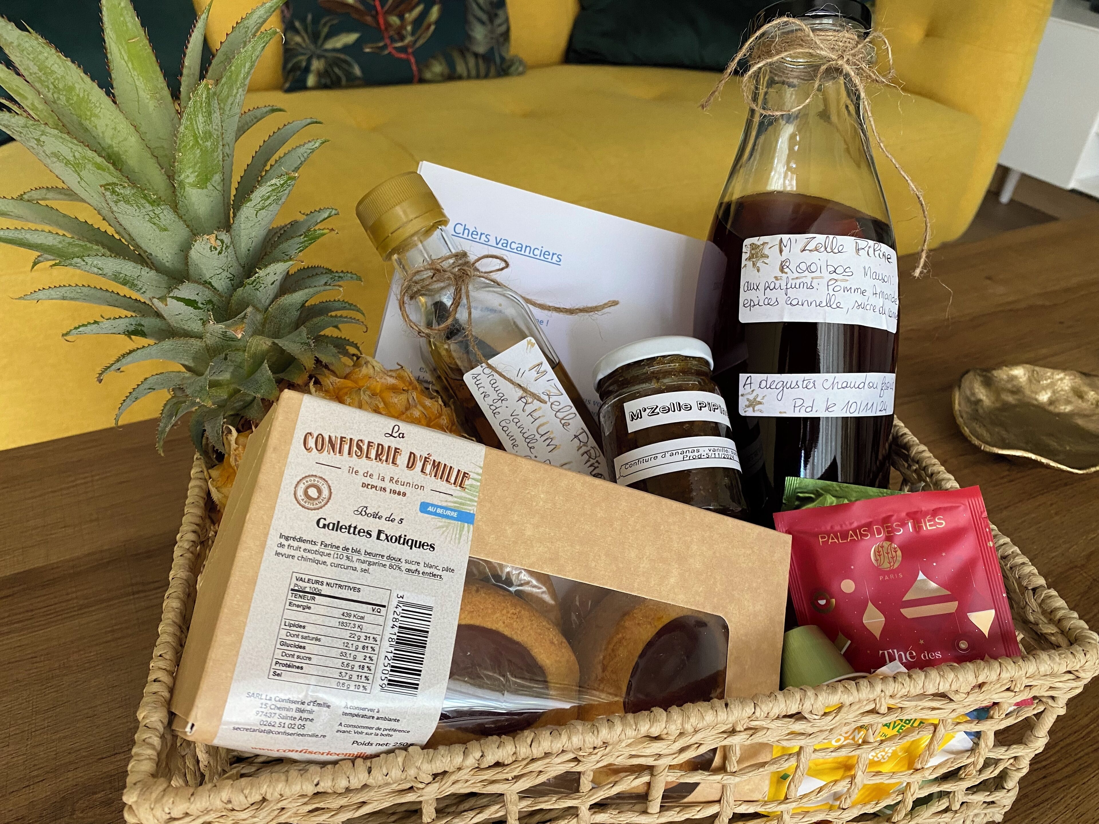 A wicker basket containing a bottle of M'Zelle Pipette, a jar of spices, a package of Galettes Exotiques, and a red packet of chocolates.