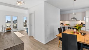 Une cuisine moderne avec des meubles blancs, une table à manger en bois et une vue sur l’extérieur.