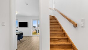 Un intérieur moderne avec un escalier en bois, un téléviseur à écran plat fixé au mur et un lit doté d’une tête de lit bleue.