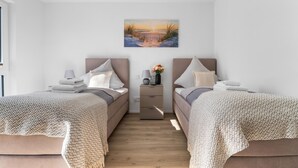 Une chambre avec deux lits, une table de chevet, une lampe et un tableau représentant un coucher de soleil sur une plage.