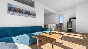 Un salon moderne avec un canapé bleu, une table basse en bois et un tableau représentant des maisons colorées accroché au mur.