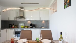 A modern kitchen with white cabinets, a built-in oven, and a dining area with two chairs and a table set for two.