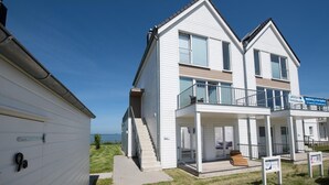 A two-story residential building with a balcony, a visible staircase, and a clear view of the sea.