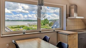 A kitchen with a large window overlooking a river, a dining table, and cabinets. - Cozy apartment in Boren with sauna (Boren)