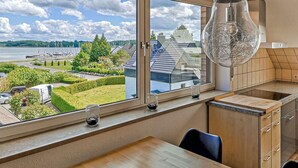 A modern kitchen with a large window overlooking a scenic waterfront view, a unique light fixture, and a minimalist design. - Cozy apartment in Boren with sauna (Boren)