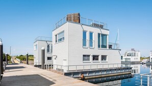 Un moderno edificio sul lungomare con tetto piano, ampie finestre e un molo che si protende sull'acqua.