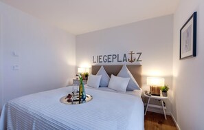 Une chambre d’hôtel avec un lit, des tables de chevet, une pancarte fixée au mur portant l’inscription « LIEGEPLATZ », et un tableau encadré accroché au mur.