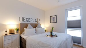 Un dormitorio ordenado con cama, mesitas de noche, una ventana y un cartel en la pared.