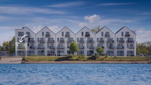 Un edificio residencial moderno de varios pisos con balcones, cerca de una masa de agua.