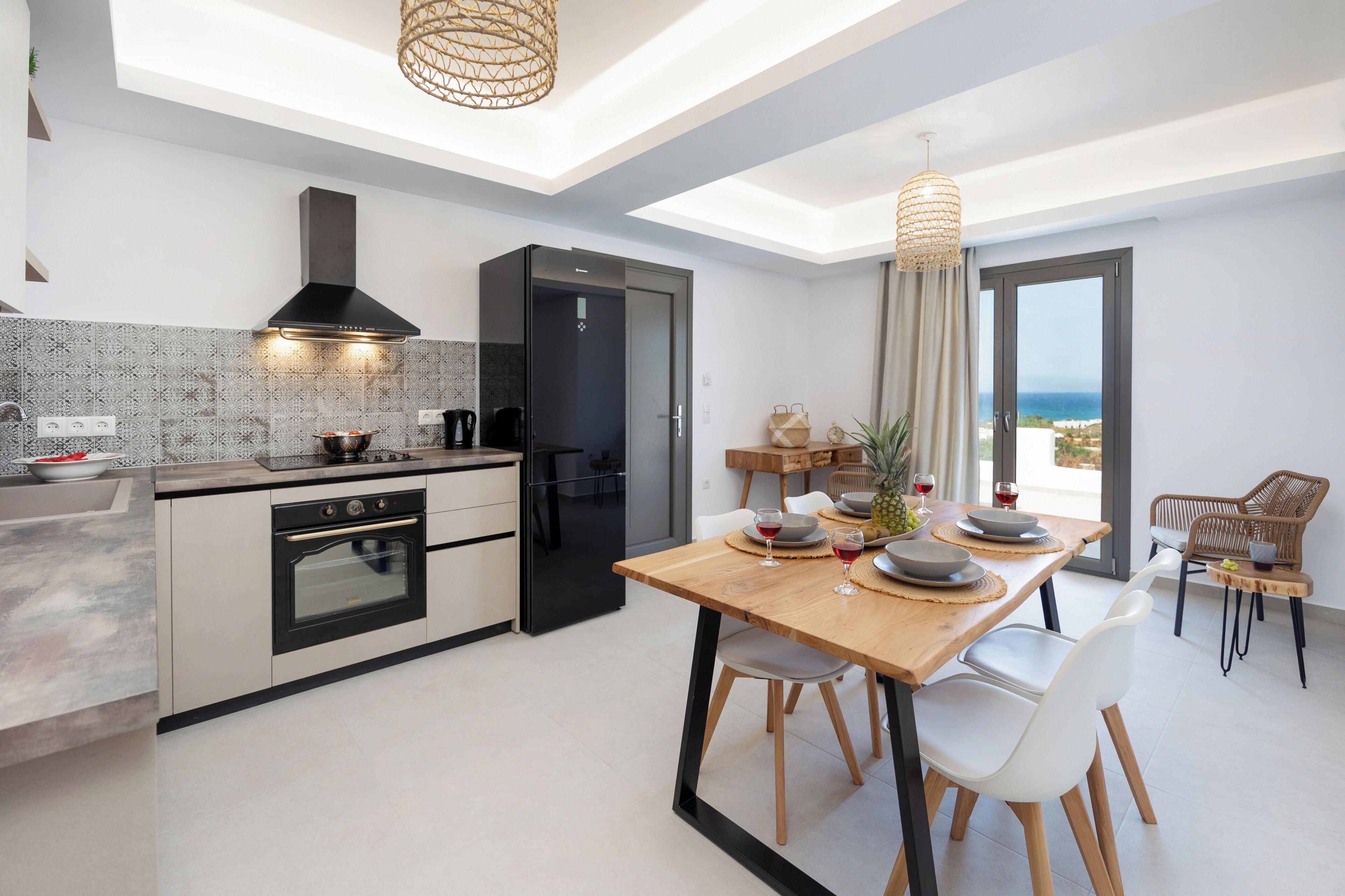 Une cuisine moderne avec un coin repas, comprenant un grand îlot central, un four encastré et une vue sur la mer par la fenêtre.