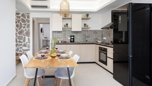 A modern kitchen with a dining area, featuring a wooden table, white chairs, a black refrigerator, and a stone accent wall. - BLUE SEA NAXOS  (Naxos)
