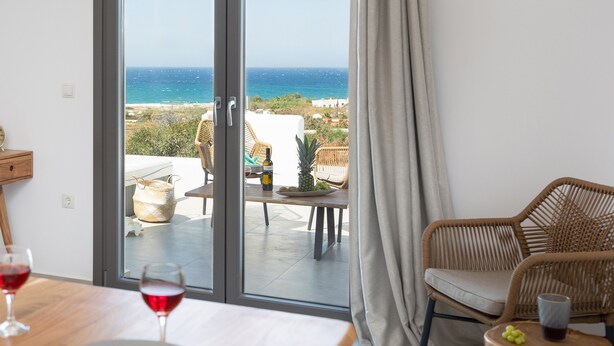 A room with a sliding glass door leading to a balcony with a view of the sea. There are wicker chairs and a table with a bottle and glasses on it. - BLUE SEA NAXOS  (Naxos)