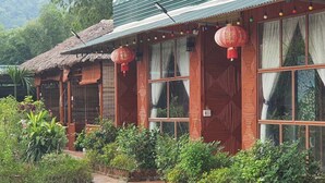 A traditional wooden building with large windows and red lanterns, surrounded by lush greenery. - HaGiang Eco Bungalow (Ha Giang 1)