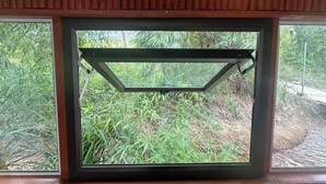 A window with a metal frame and a view of dense greenery outside. - HaGiang Eco Bungalow (Ha Giang 1)