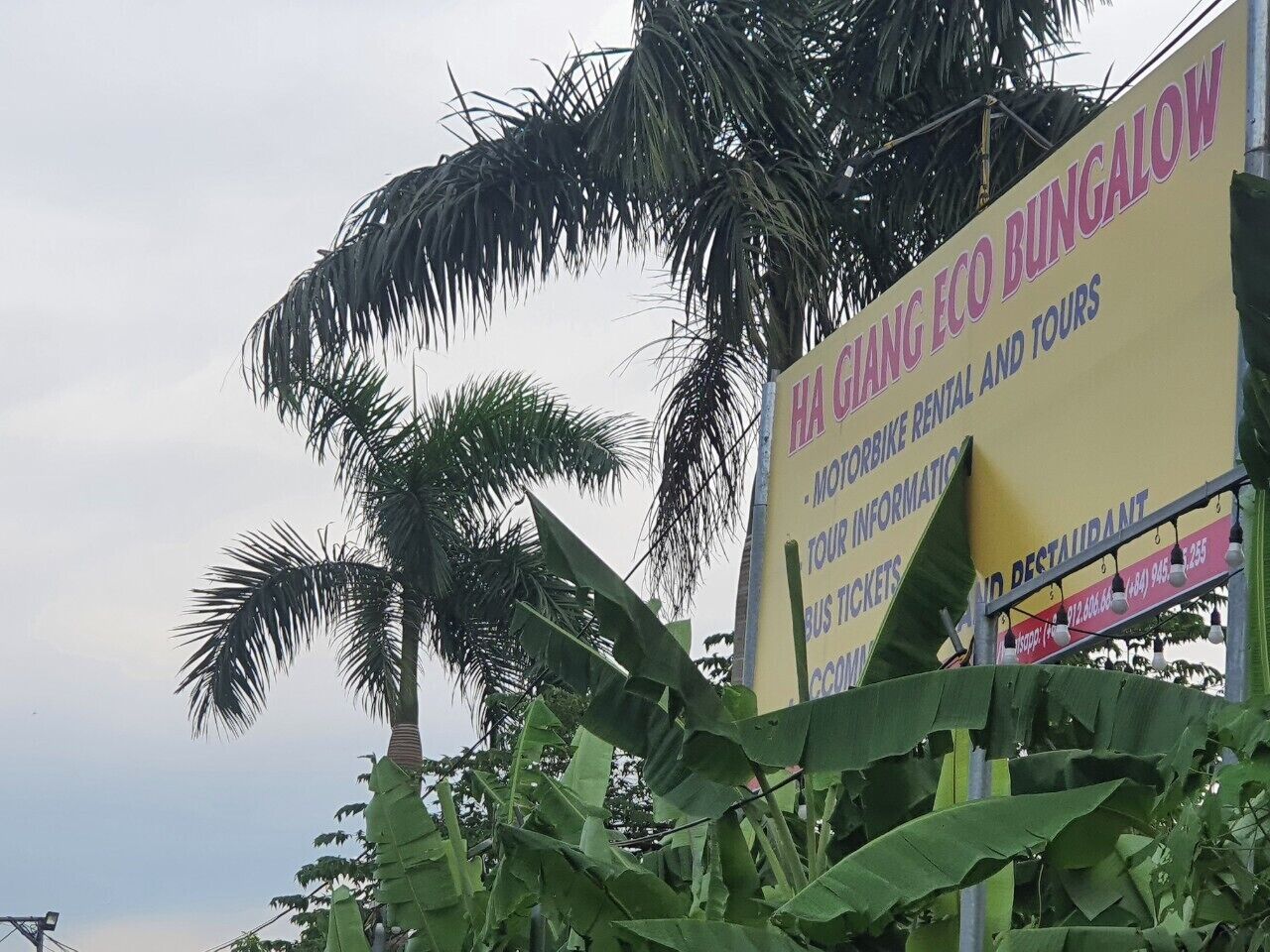 A sign for Ha Chiang Eco Bungalow advertising motorbike rental, tour information, bus tickets, and a restaurant.