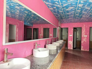Ett badrum med rosa väggar, en lång bänkskiva med handfat och ett tak som är målat för att likna en himmel med moln.