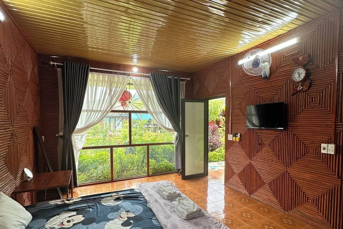 A room with a bed, a TV, a fan, and a window with curtains.