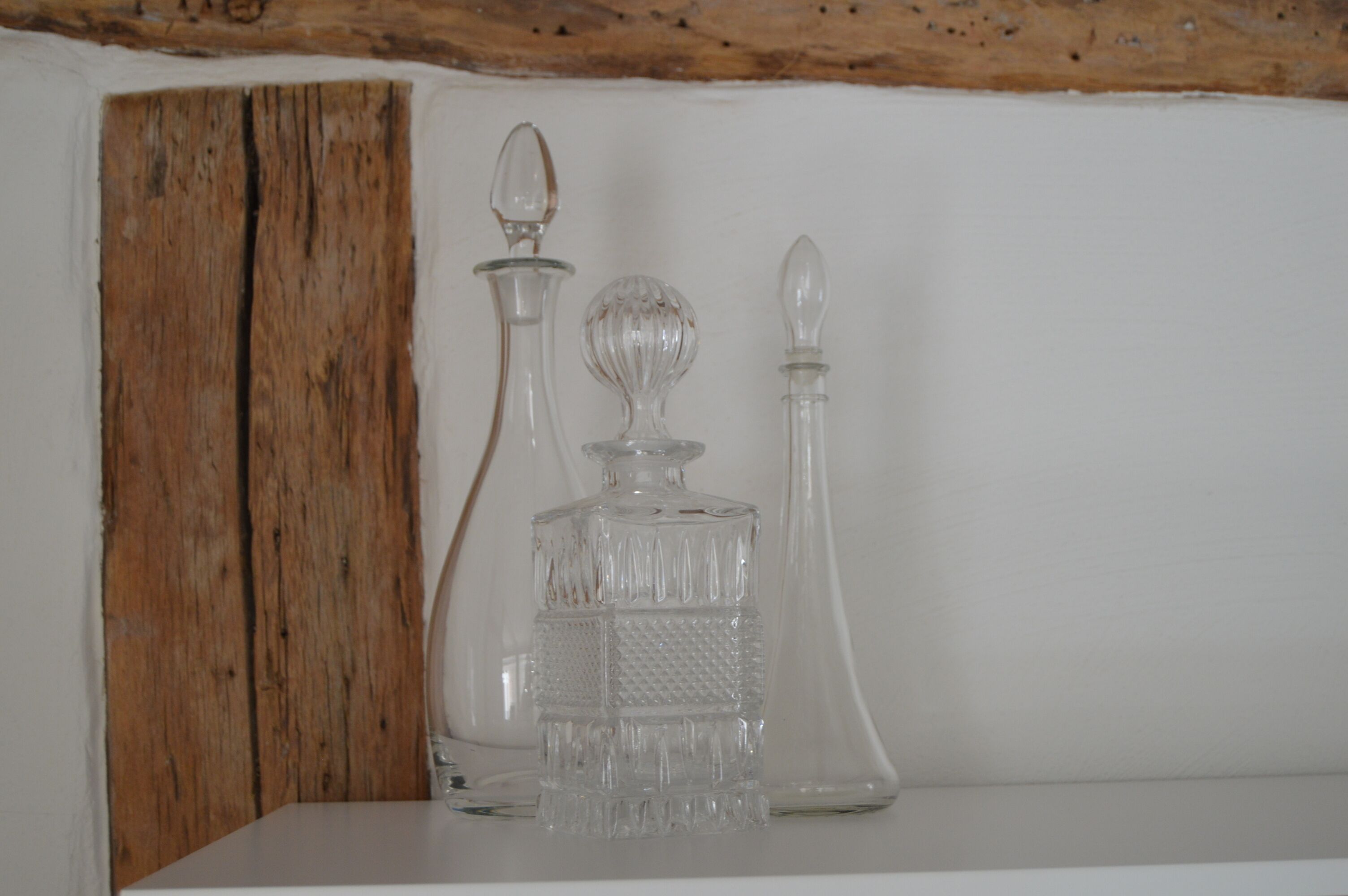 Three glass decanters on a white shelf against a wooden wall.