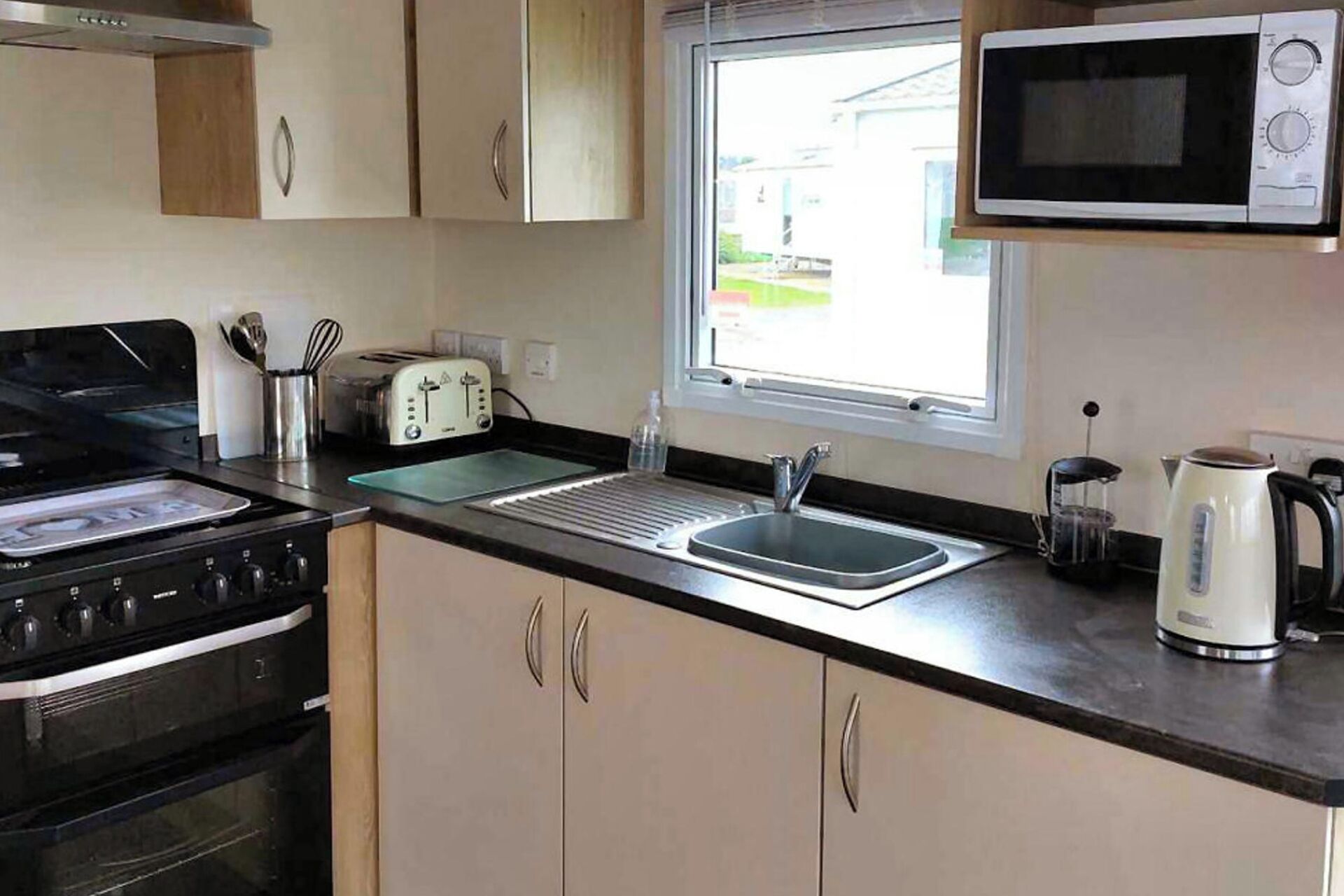 A kitchen with a stove, toaster, sink, microwave, and a window.