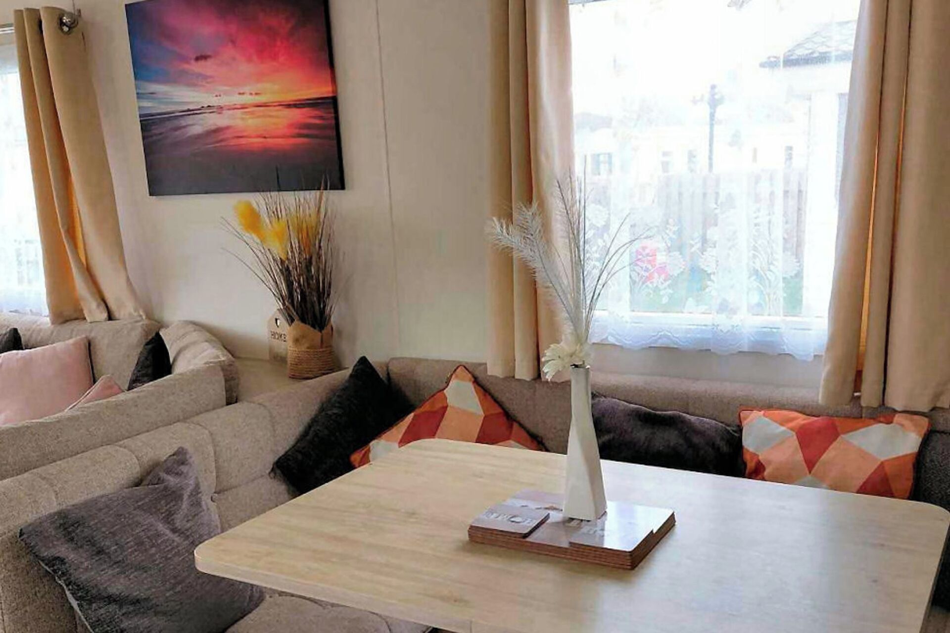 Una sala de estar con un sofá, una mesa con un florero y libros, y un cuadro en la pared.